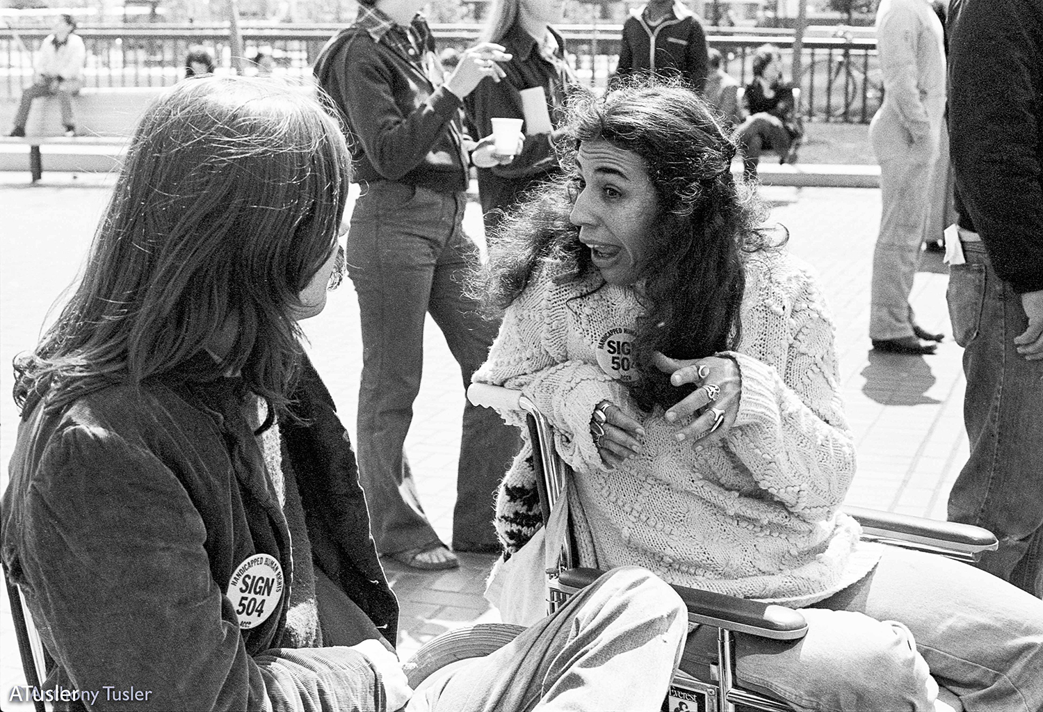 Black and white photo of two people in manual wheelchairs talking to each other.