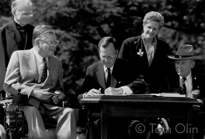 Black and white photo of the President signing a document with others smiling around him